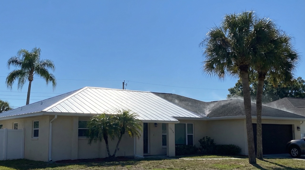 Bright, light-colored reflective cool roof on a Clearwater home on a sunny day, showing contrast with dark heat-absorbing traditional roofing, palm trees, and blue sky.